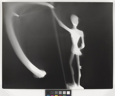 An abstract black-and-white photograph of an illuminated white figure and blurred lights against a black background.