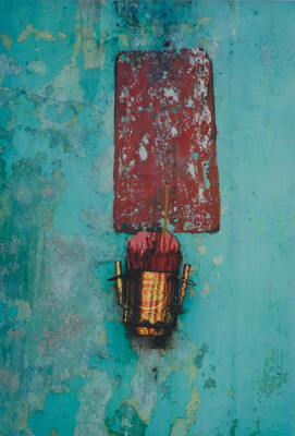 A color photograph of a textured blue wall with a dark red rectangle on which hangs a metallic bucket of incense.