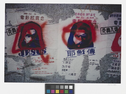 A color photograph of torn flyers printed with images of Jesus on what looks like a concrete wall; red markings are spray painted over the flyers.