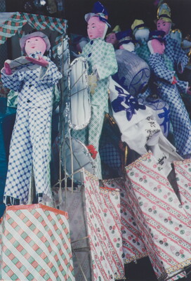 A color close-up photograph of a group of dolls or puppets wearing checked clothing piled against one another.