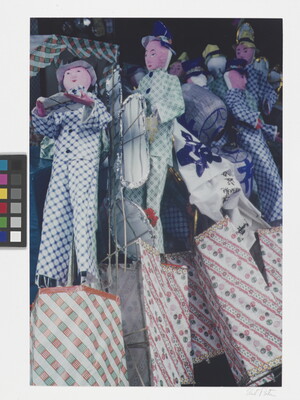 A color close-up photograph of a group of dolls or puppets wearing checked clothing piled against one another.