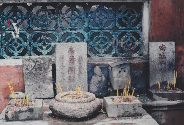 A color photograph of a shrine on a stone altar with incense sticks in stone holders of varying shapes.
