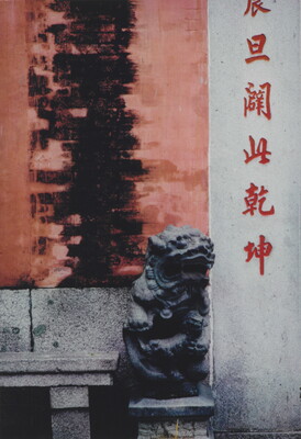 A color photograph of a black stylized stone animal statue sitting on a column in front of a wall covered with Asian characters.