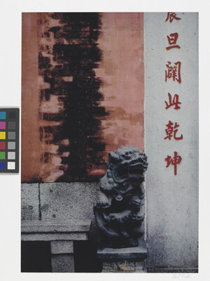 A color photograph of a black stylized stone animal statue sitting on a column in front of a wall covered with Asian characters.