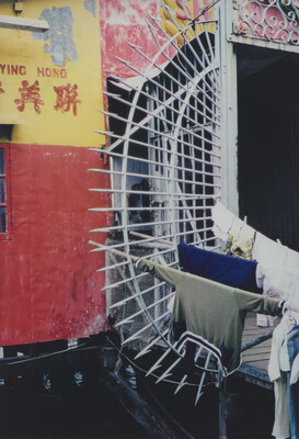 A color photograph of a wall painted red and yellow next to a white metal gate on which hangs some laundry.