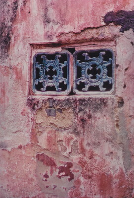 A color photograph of a red plaster wall containing two decorative window grates.