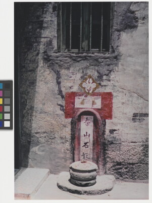 A color photograph of a shrine inset in a plaster wall, red and white geometric details are painted on the wall,  a cylindrical incense burner sits in front of it.