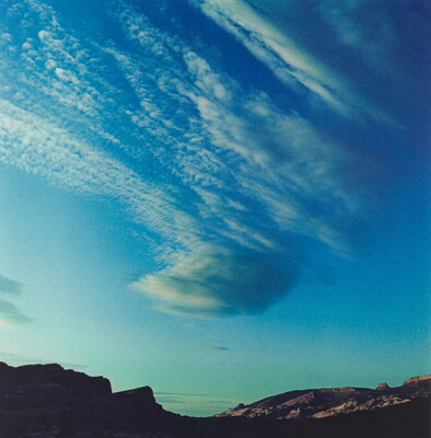 A color photograph of radiatus white clouds in a blue sky over a rocky landscape.