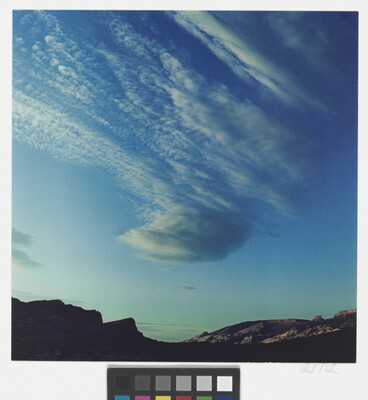 A color photograph of radiatus white clouds in a blue sky over a rocky landscape.