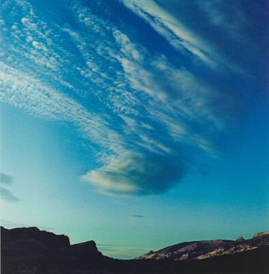 A color photograph of radiatus white clouds in a blue sky over a rocky landscape.