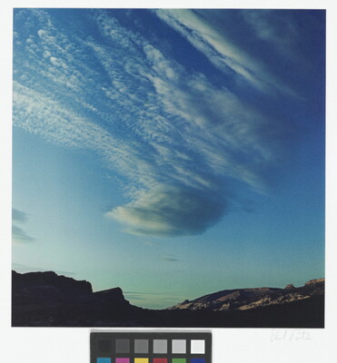 A color photograph of radiatus white clouds in a blue sky over a rocky landscape.