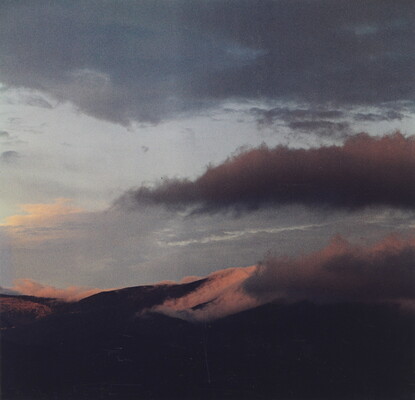 A color photograph of a mountain range with clouds in a blue and pink sky.