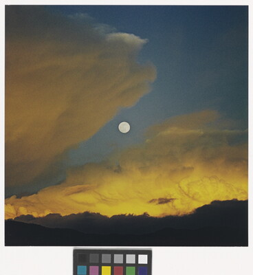 A color photograph of a full moon in a dark blue sky with yellow swirling clouds.