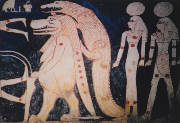 A color photograph of a mural with white and red hieroglyphs featuring what looks like a lion walking upright, a crocodile climbing on its back, and two people with circles over their heads.