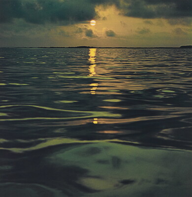A color photograph of a sunset reflected over a calm, dark ocean.