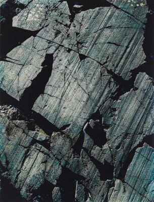 A color close-up photograph of dark gray rocks with diagonal striations and cracks.