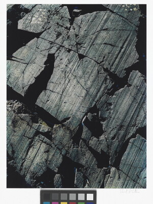 A color close-up photograph of dark gray rocks with diagonal striations and cracks.