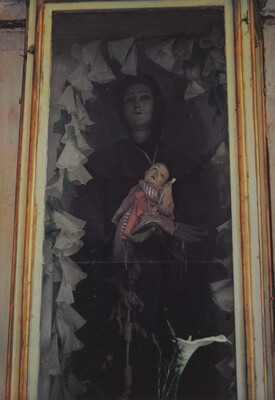 A color photograph of a sculpture of a female figure holding a baby recessed into a wall.