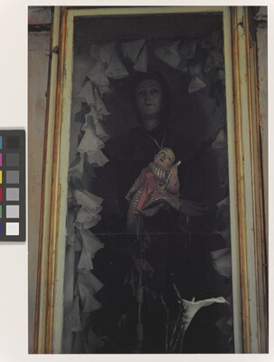 A color photograph of a sculpture of a female figure holding a baby recessed into a wall.