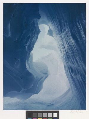 A color photograph taken inside an ice cave with swirling blue walls and a bright opening toward daylight.