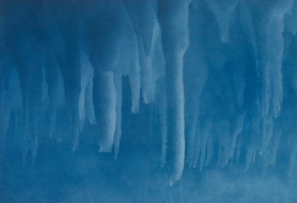 A color photograph taken inside an ice cave with deep blue stalactites hanging from the ceiling.