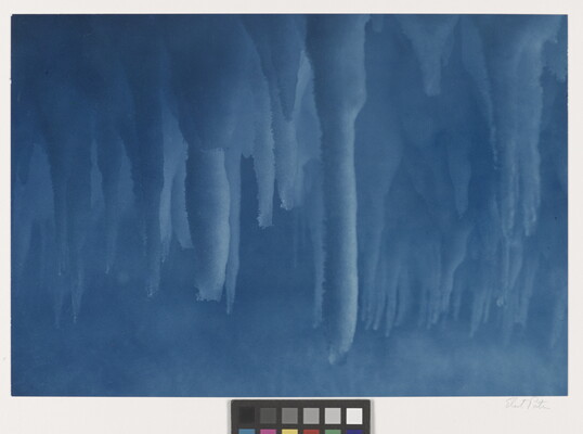 A color photograph taken inside an ice cave with deep blue stalactites hanging from the ceiling.