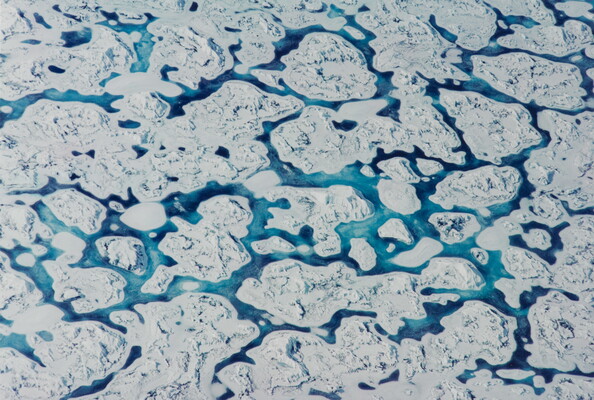 A color aerial photograph of white ice floes with ribbons of blue water running through them.