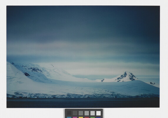A color photograph of a snowy coastline with mountains and dense clouds.