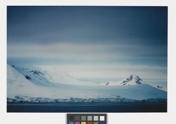 A color photograph of a snowy coastline with mountains and dense clouds.