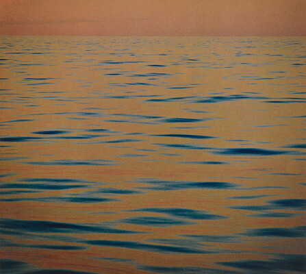 A color photograph of calm ripples of the sea at sunset reflecting an orange-red sky.