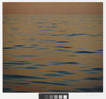A color photograph of calm ripples of the sea at sunset reflecting an orange-red sky.