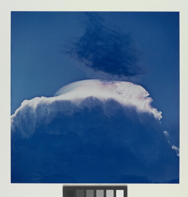 A color photograph of a large storm cloud with a striking white top and dark blue base.
