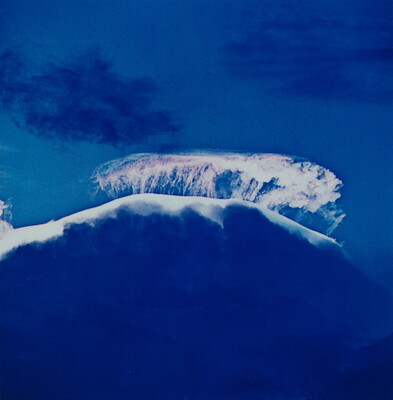 A color photograph of a large storm cloud with a striking white top and dark blue base.