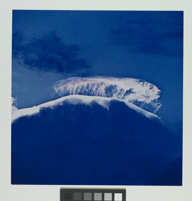A color photograph of a large storm cloud with a striking white top and dark blue base.