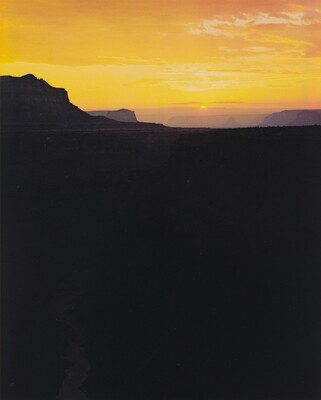 A color photograph of dark black and purple canyon walls in silhouette beneath a bright yellow and orange sunrise.