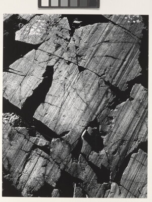 A color close-up photograph of dark gray rocks with diagonal striations and cracks.