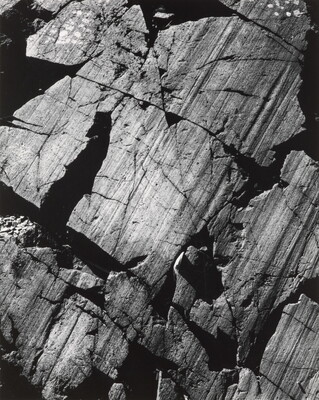 A color close-up photograph of dark gray rocks with diagonal striations and cracks.