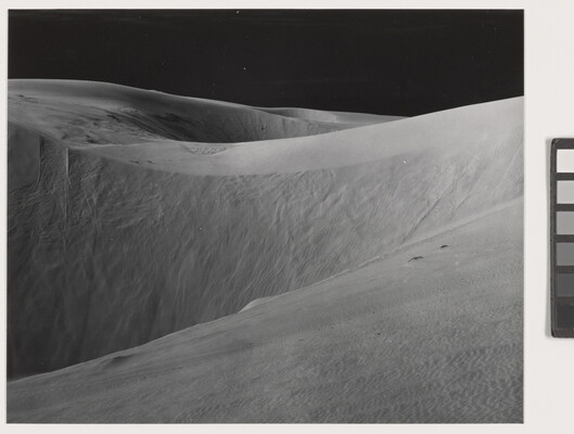 A black-and-white photograph of white sand dunes under a dark night sky.