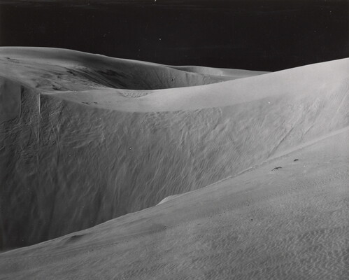 A black-and-white photograph of white sand dunes under a dark night sky.