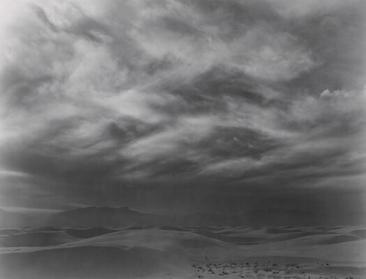 A black-and-white photograph of storm clouds forming over a desert landscape.