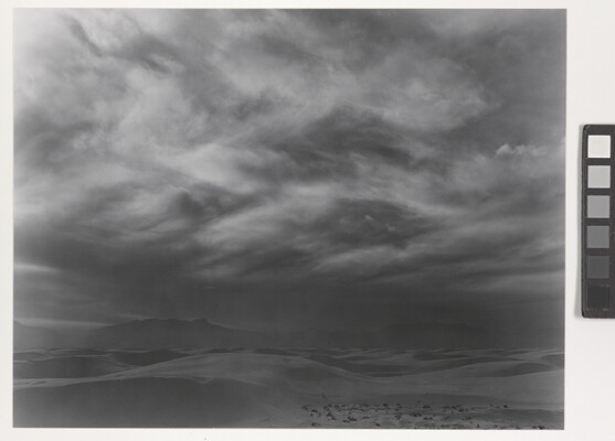 A black-and-white photograph of storm clouds forming over a desert landscape.