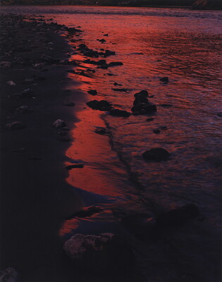 A color photograph of red-tinted waves on a dark, rocky shoreline.