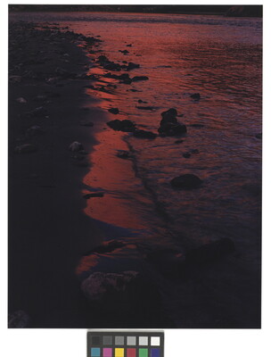 A color photograph of red-tinted waves on a dark, rocky shoreline.
