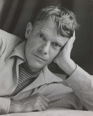 A black-and-white photograph portrait of a White man on his side, head resting on his hand, looking at the camera.