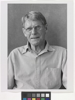 A black-and-white photograph of an older White man with short gray hair, wearing glasses and a button-down long-sleeved shirt.