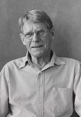 A black-and-white photograph of an older White man with short gray hair, wearing glasses and a button-down long-sleeved shirt.