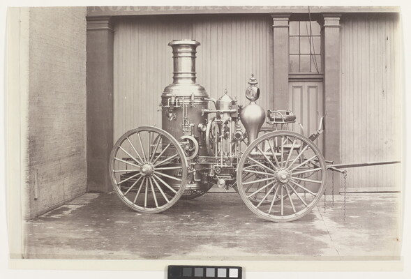 A black-and-white photograph of a parked wagon with a large tank and other mechanical features.