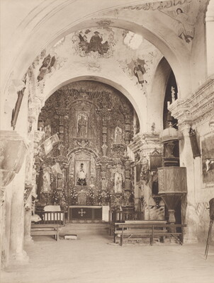 A black-and-white photograph of an ornate church interior showing arches and the altar.
