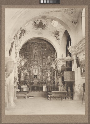 A black-and-white photograph of an ornate church interior showing arches and the altar.
