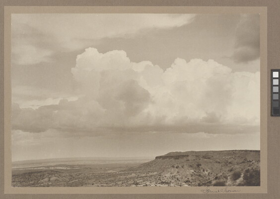 A black-and-white photograph of a mesa with a plain below it beneath a cloudy sky.